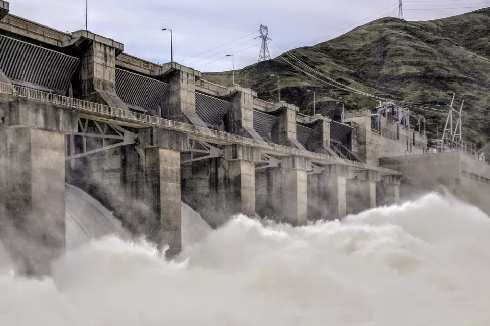 Water rushes over a spillway at a large concrete dam.